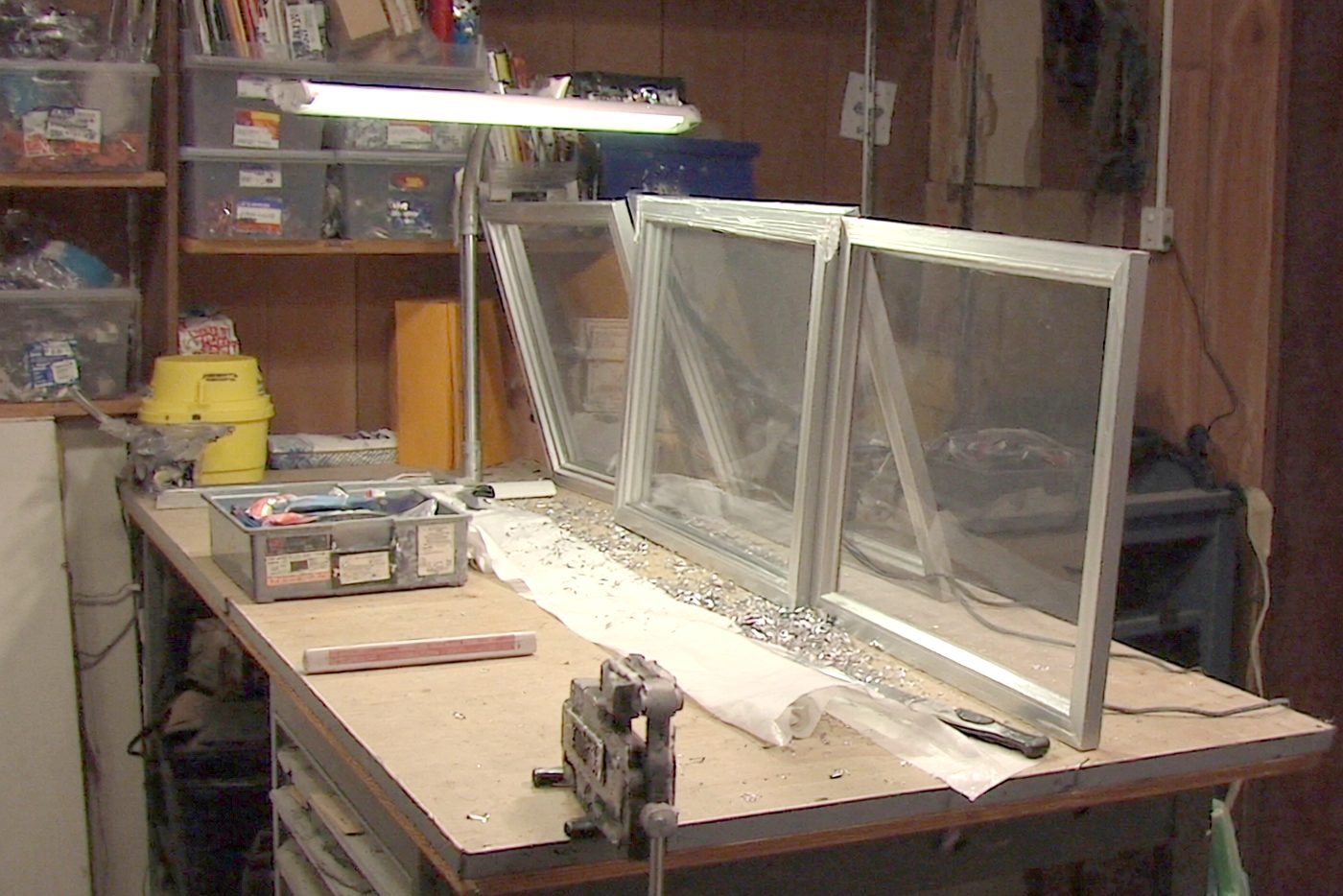 The repair bench at the back of the store, three screen frames leaning on it under a lit shop lamp, a vise clamped to the near edge.