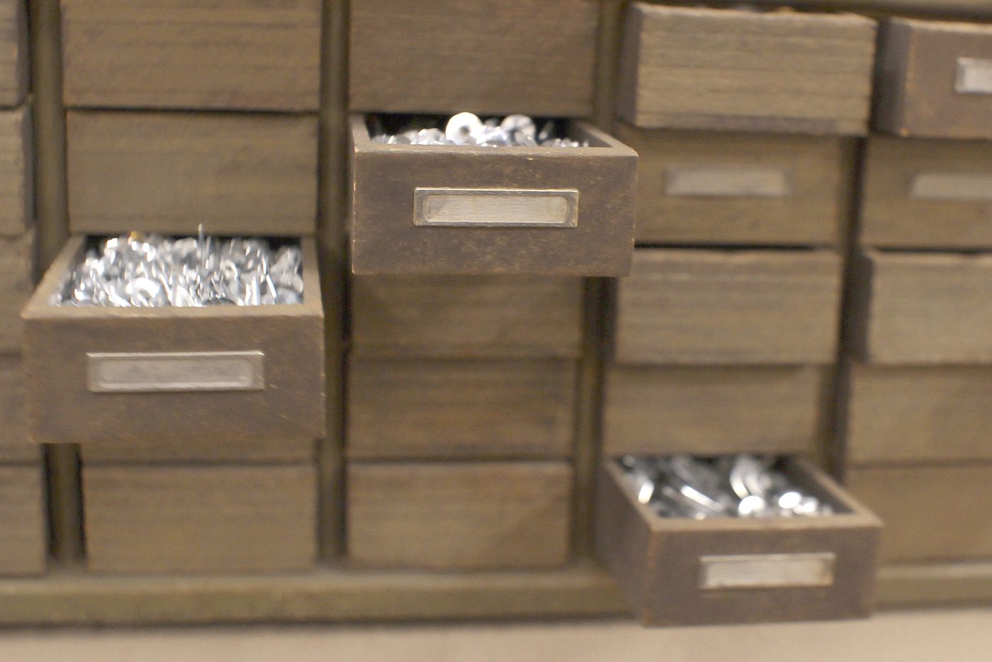 The wall of small fastener drawers, a few pulled open showing galvanized bolts, nuts and washers.