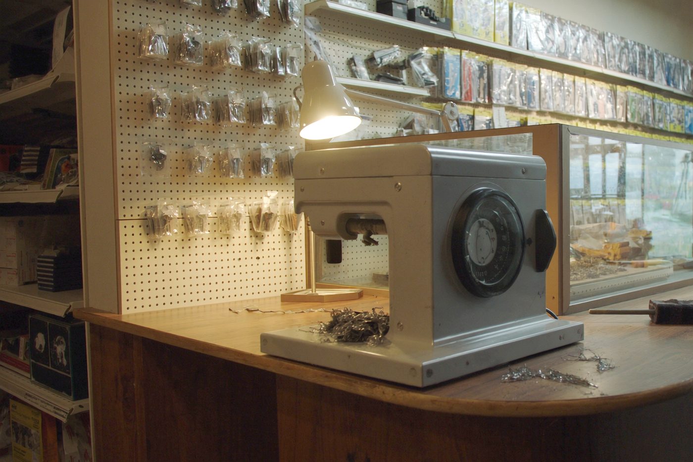 The key duplicating machine on the counter, a pegboard of blanks behind it, a work lamp switched on above.